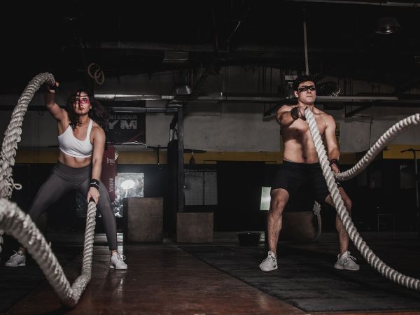 um homem e uma mulher praticando exercícios com corda naval em um box de crossfit