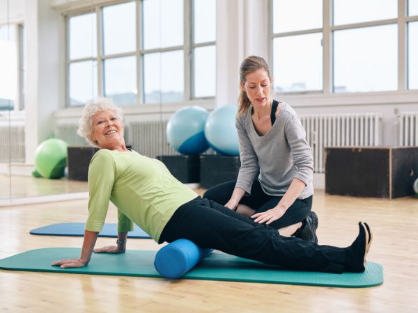 mulher idosa praticando pilates de solo com auxílio de uma personal trainer