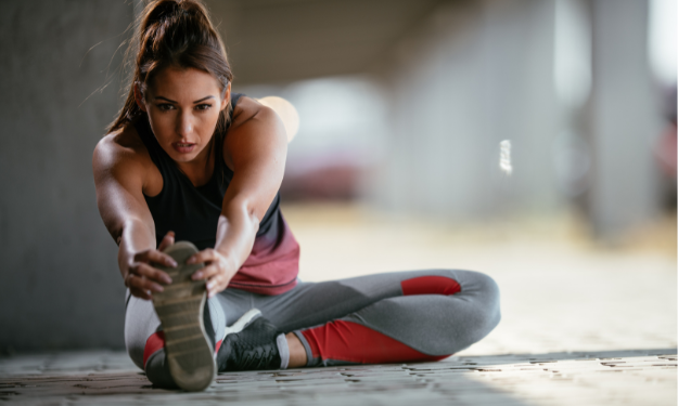 Mulher realizando exercício de alongamento sentada no chão, para as pernas.