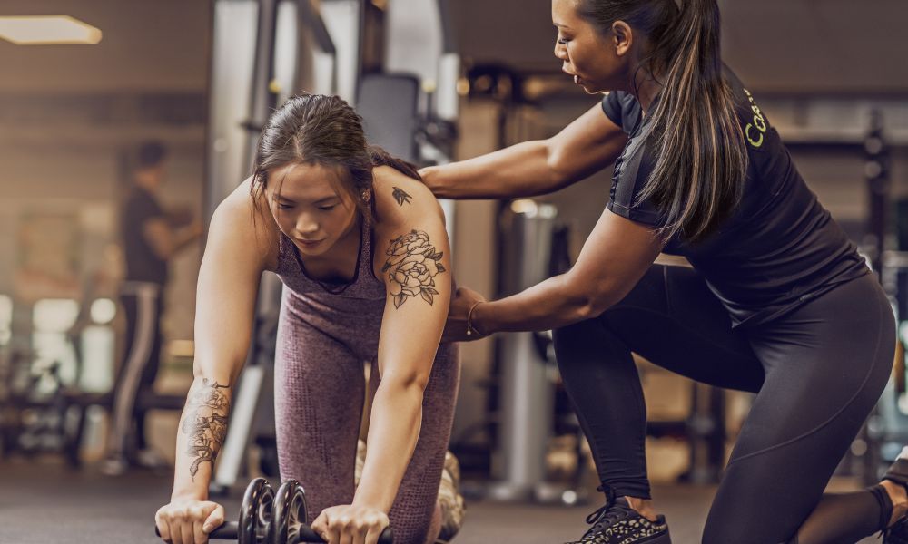 Personal trainer dando assistência para uma aluna em uma academia.